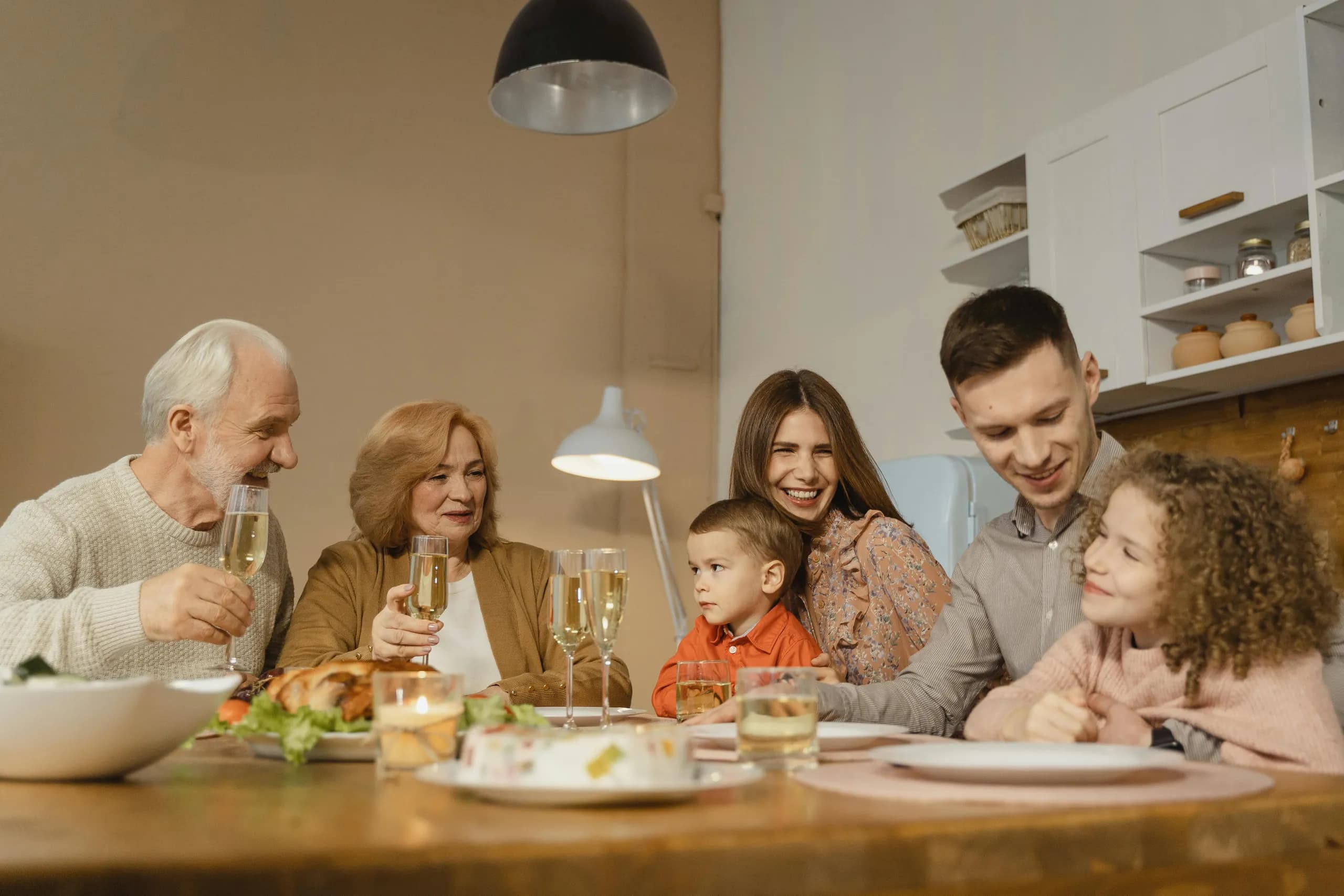 Three generations of a family gathered around the dinner table, smiling and toasting over a meal