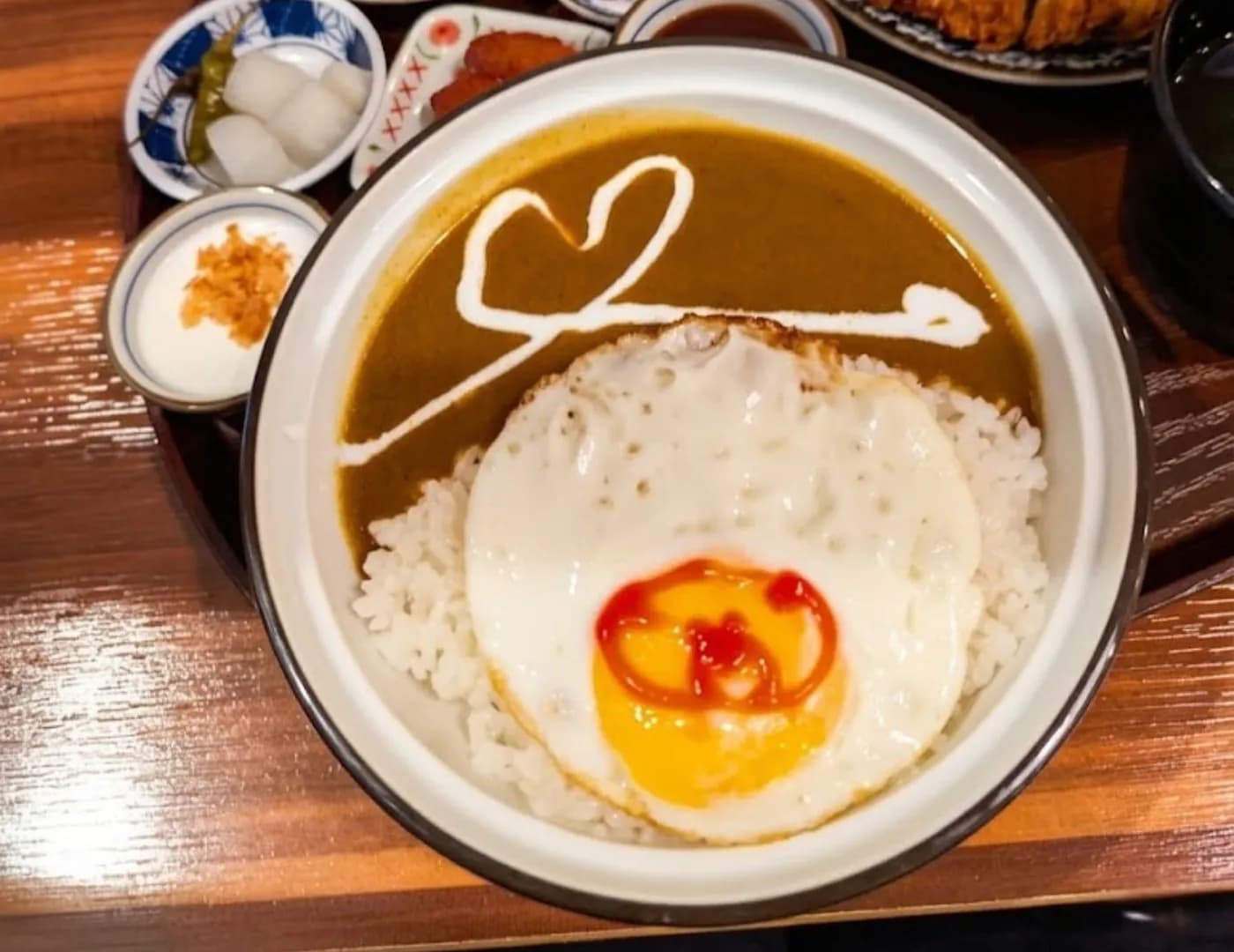 Bowl of Japanese curry rice topped with a fried egg, with pickles and a cutlet on the side