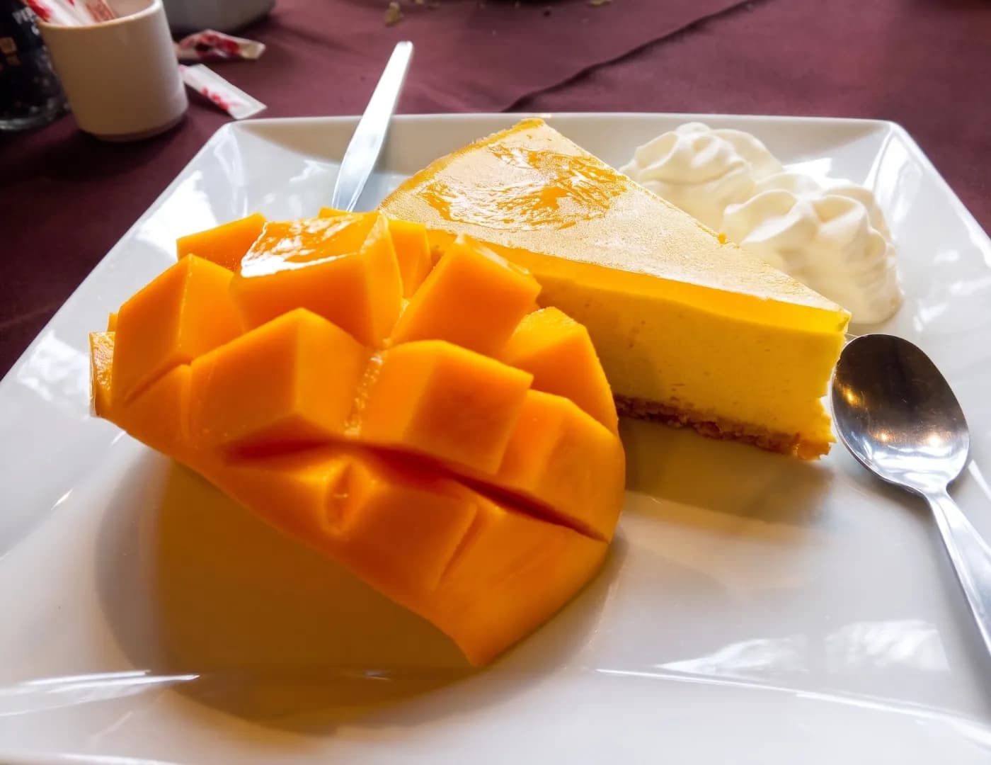 Plate of fresh sliced mango beside a slice of mango cheesecake topped with cream