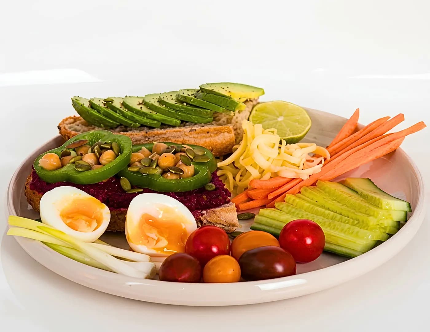 Plate of avocado and beetroot-hummus toast with a boiled egg, chickpeas, carrot, cucumber and cherry tomatoes