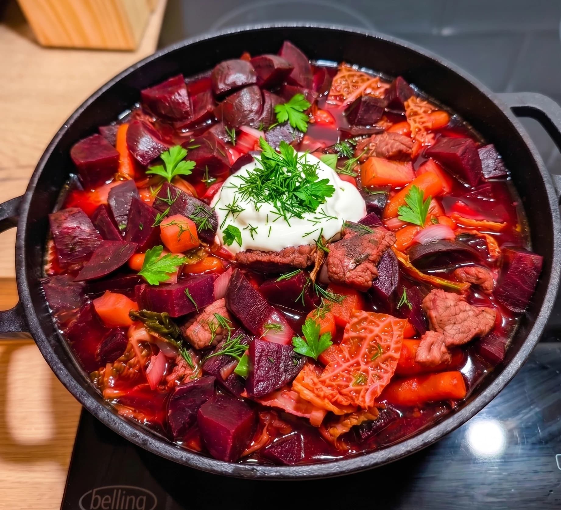 Pan of beetroot-and-beef borscht topped with a spoon of sour cream and fresh dill
