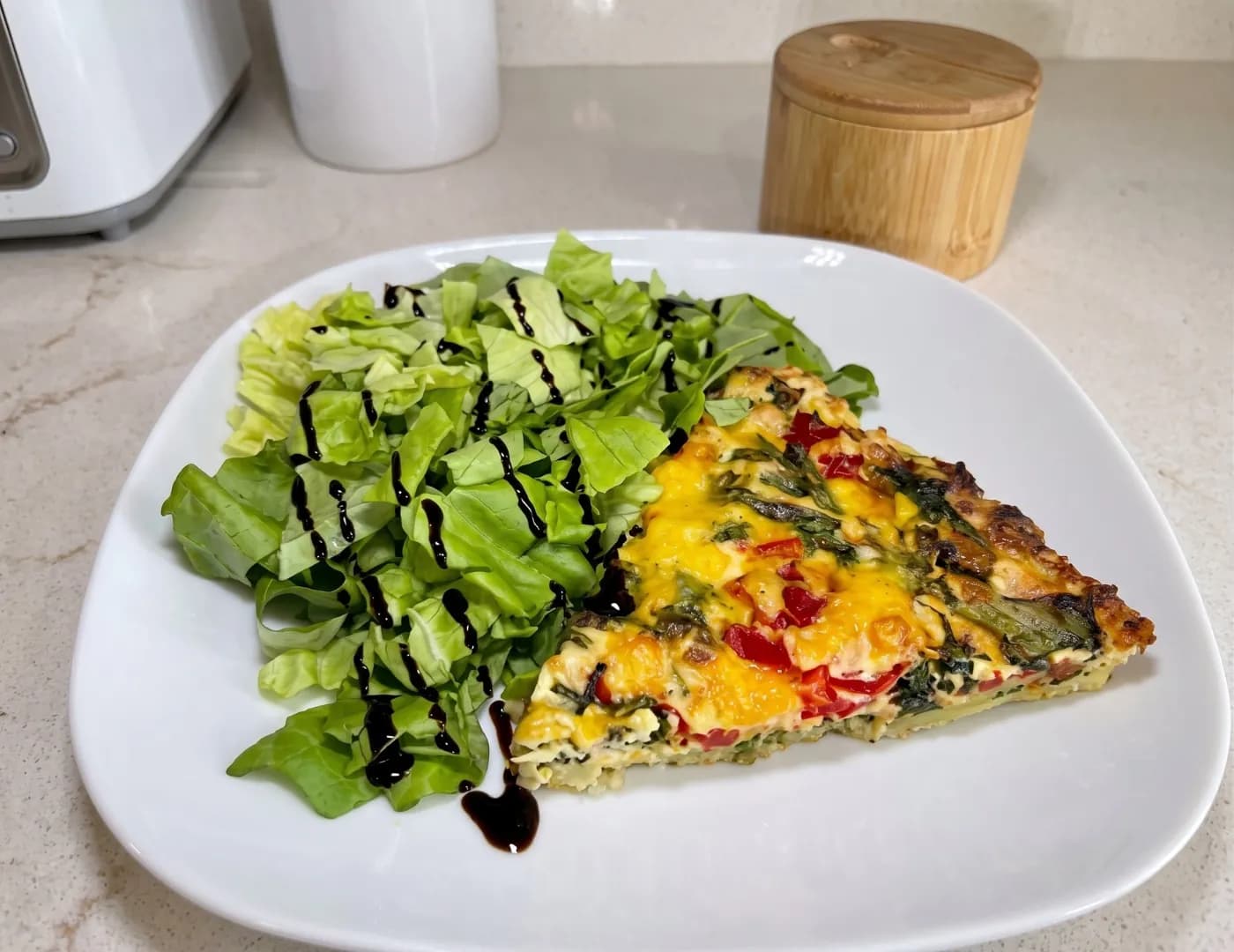 Slice of vegetable frittata with red pepper and greens, beside a balsamic-dressed salad