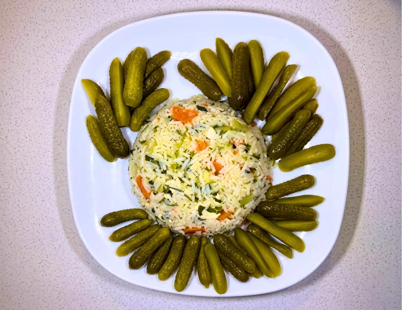Plate of herbed carrot rice salad ringed with whole gherkins