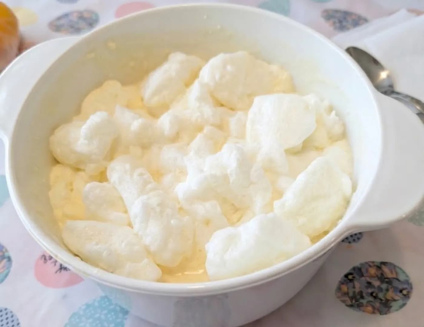 White bowl of soft whipped foam over a pale custard, with a spoon