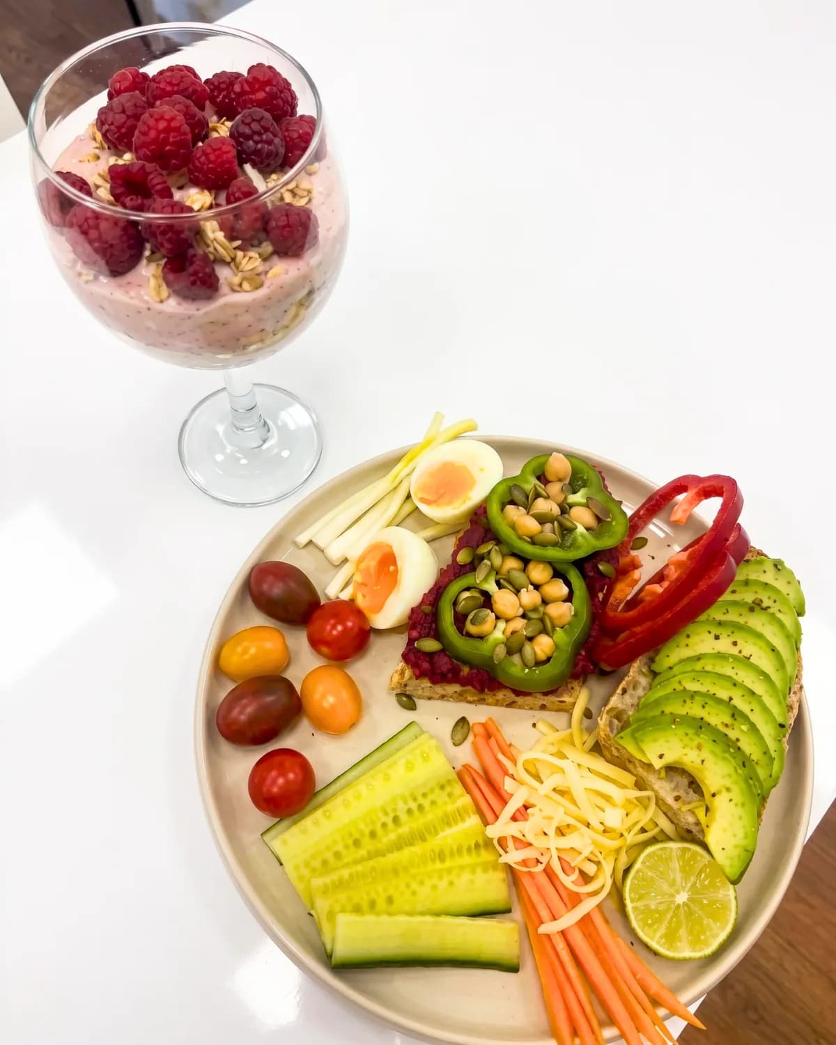 Raspberry parfait glass beside a crudité plate with avocado, egg, carrot, cucumber and lime