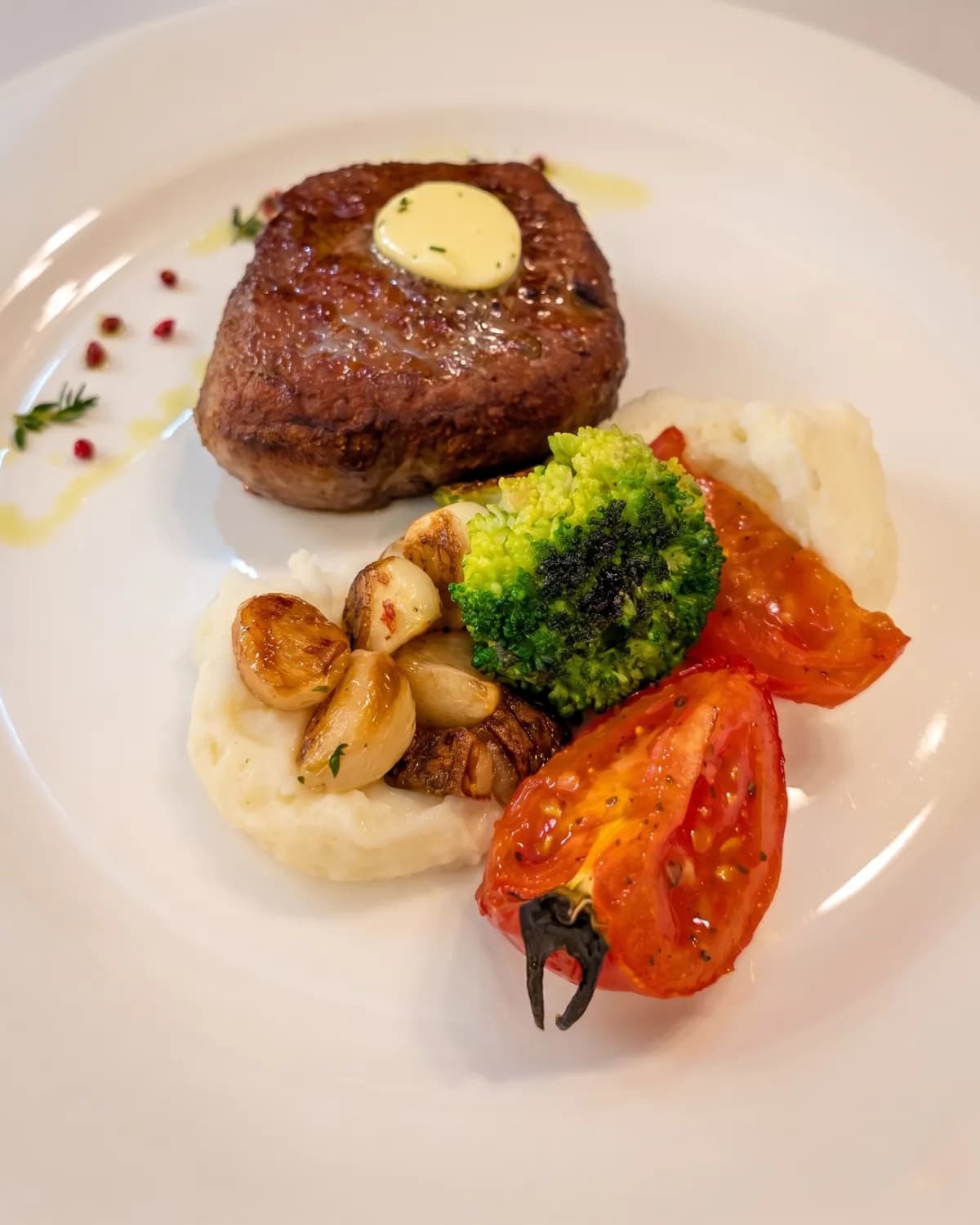 Plated steak medallion with herb butter, mashed potato, mushrooms, broccoli and roasted tomato