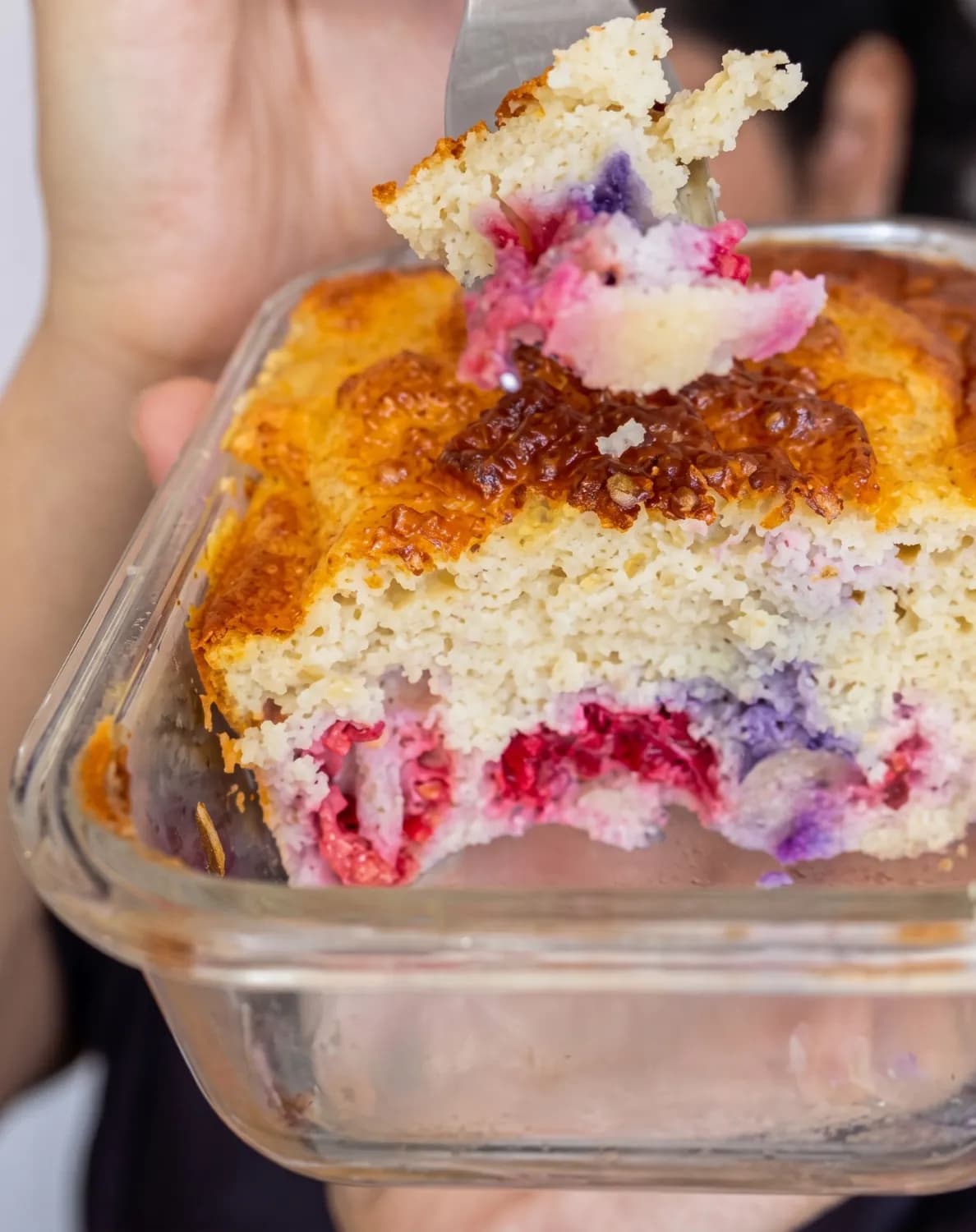 Hands holding a glass dish of baked sponge cake with a berry filling