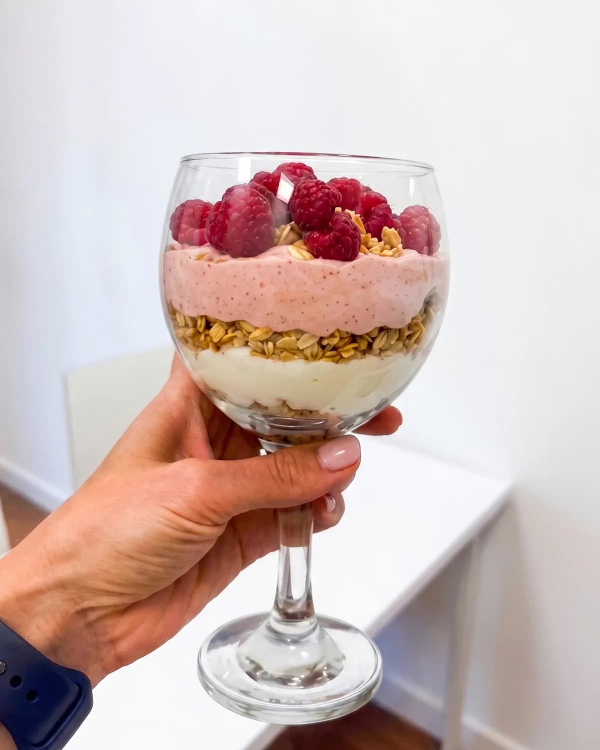 Hand holding a glass of raspberry parfait layered with granola
